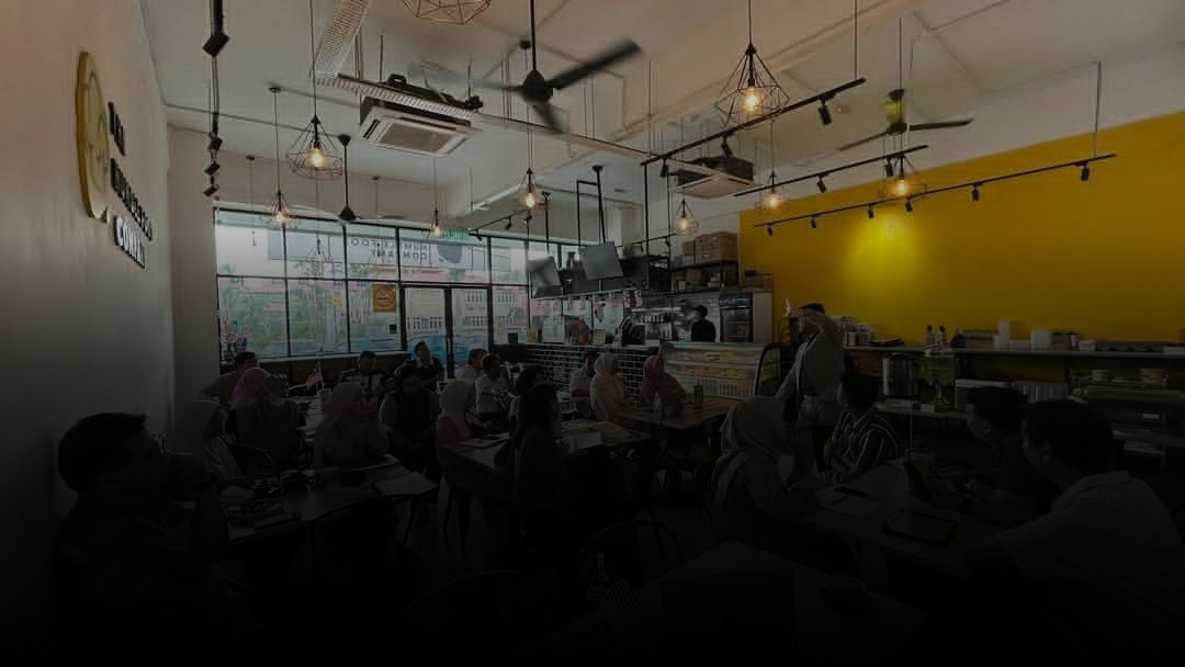 Cikgu Fazlan standing and guiding a full cafe workshop of entrepreneurs